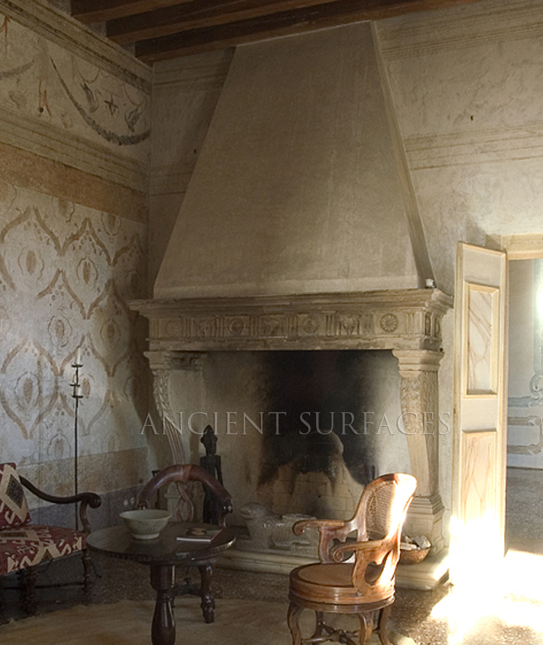 Monumental reclaimed Italian Renaissance limestone chimneypiece from Ancient Surfaces with a tapering hood and carved rosette frieze, in a frescoed room under exposed beams