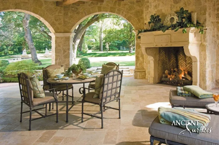 Pale golden reclaimed limestone fireplace mantel from Ancient Surfaces with a raised centre tablet, alight in an arcaded garden loggia overlooking clipped topiary
