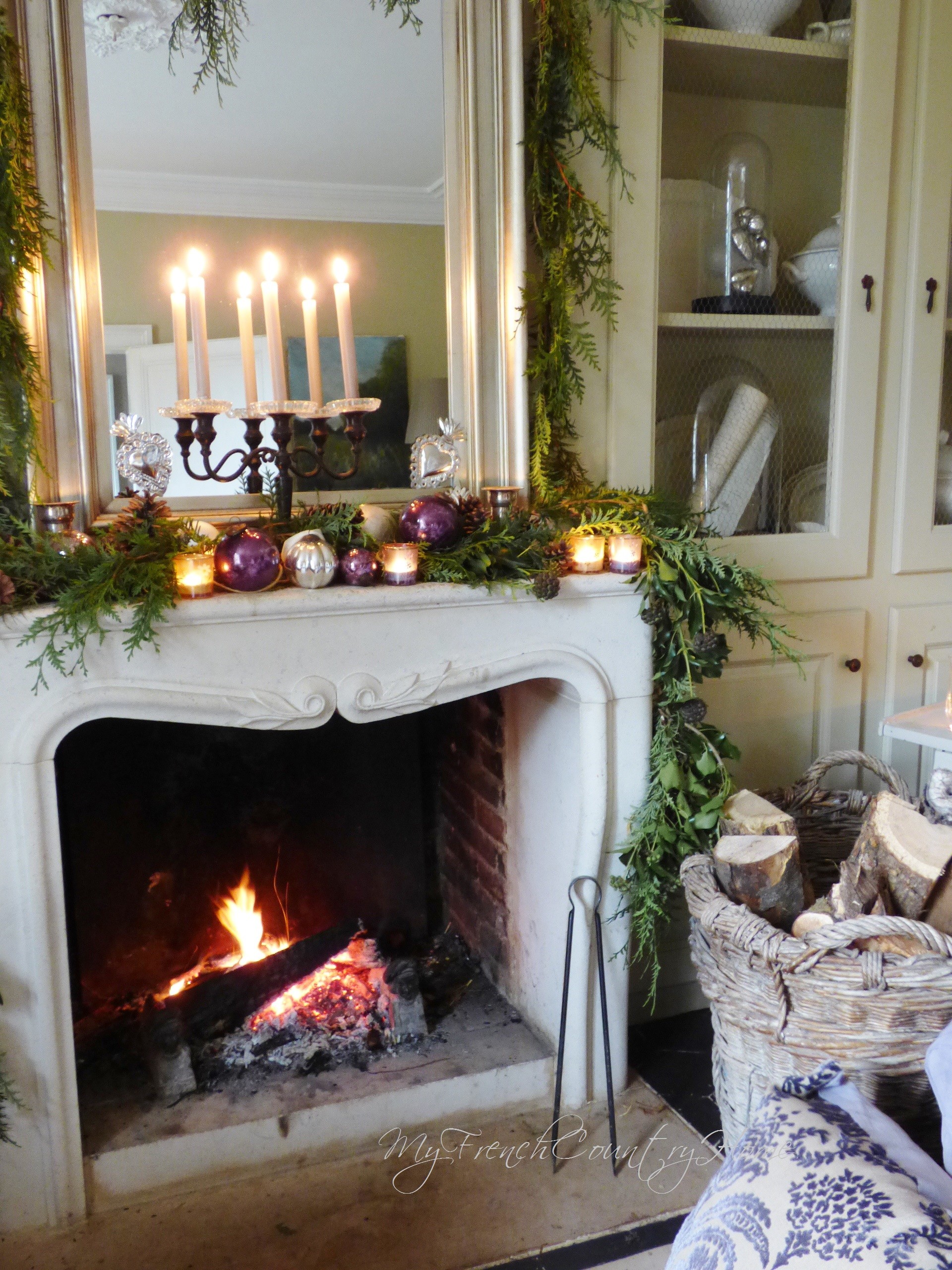 Small reclaimed Louis XV limestone fireplace mantel from Ancient Surfaces with a serpentine shelf and carved acanthus scroll, lit in a French country room below a silvered mirror