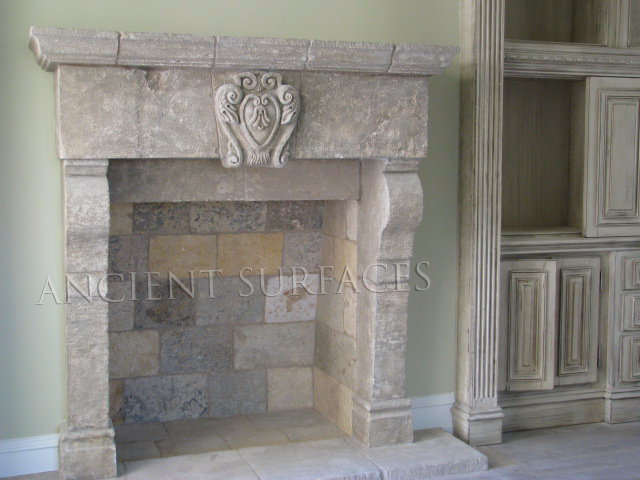 Reclaimed antique French limestone fireplace mantel from Ancient Surfaces with a carved shield cartouche on a plain frieze, photographed straight on beside painted joinery
