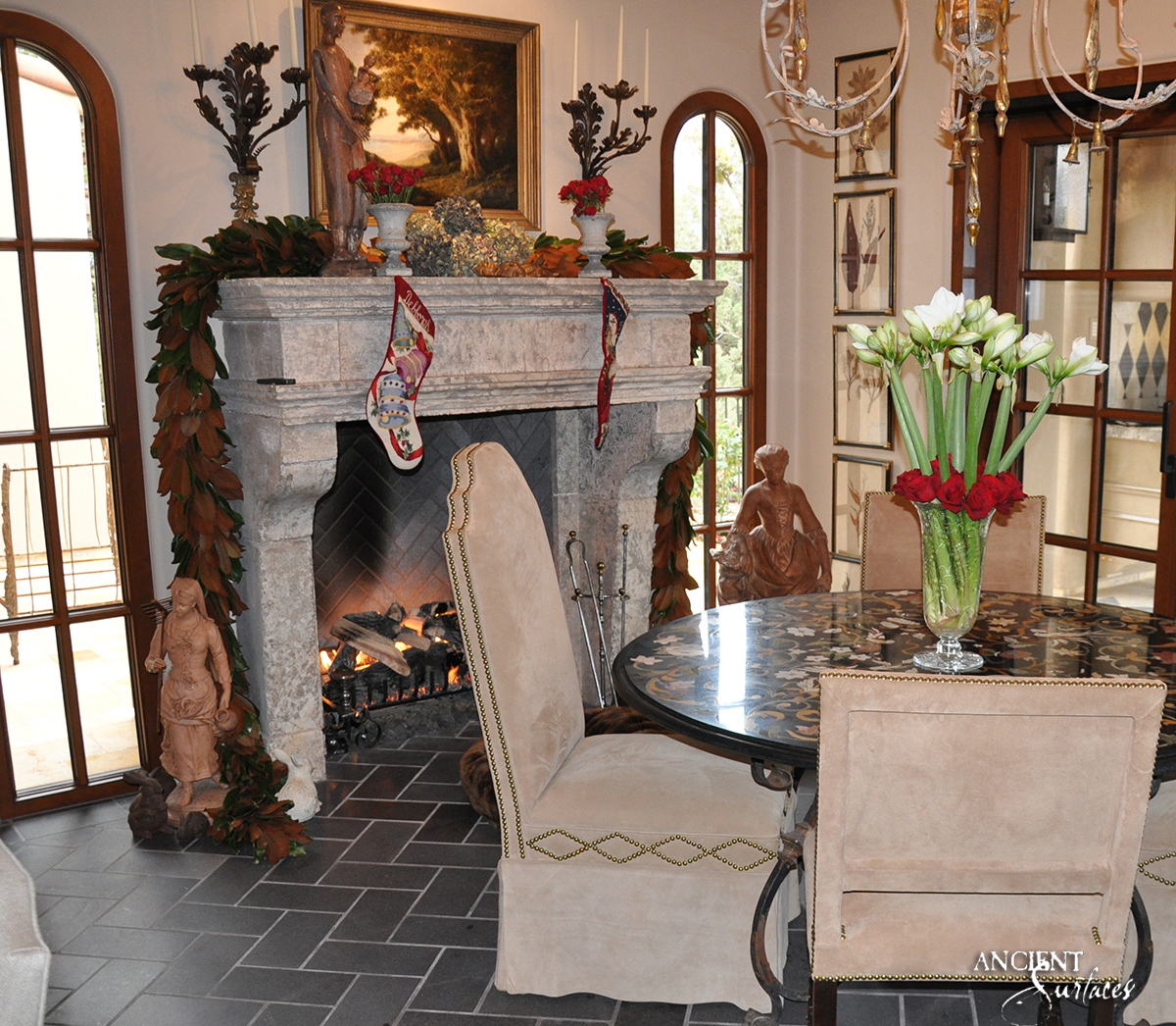 Heavily weathered grey reclaimed limestone fireplace mantel from Ancient Surfaces with scrolled corbels, burning in a dining room with arched doors and a slate herringbone firebox